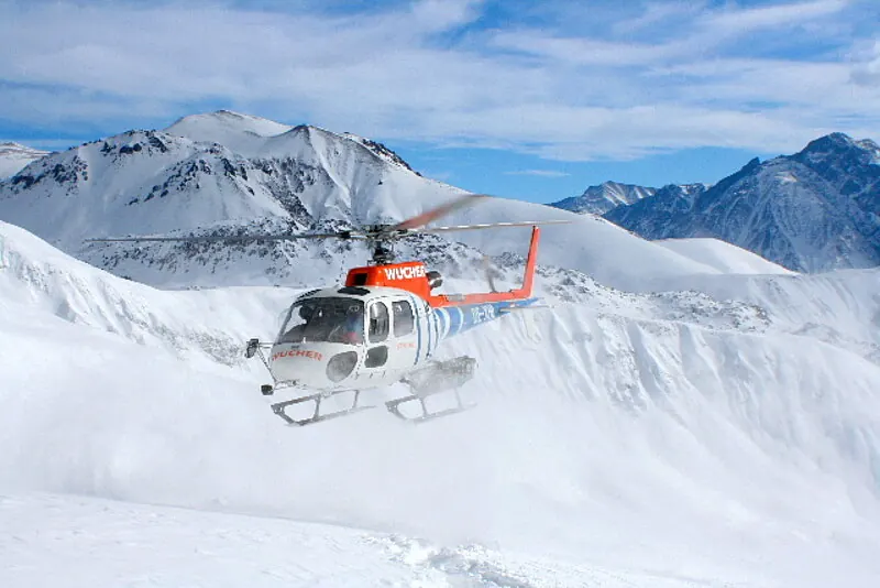 Hubschrauber landet im Schnee vor verschneiten Gipfeln